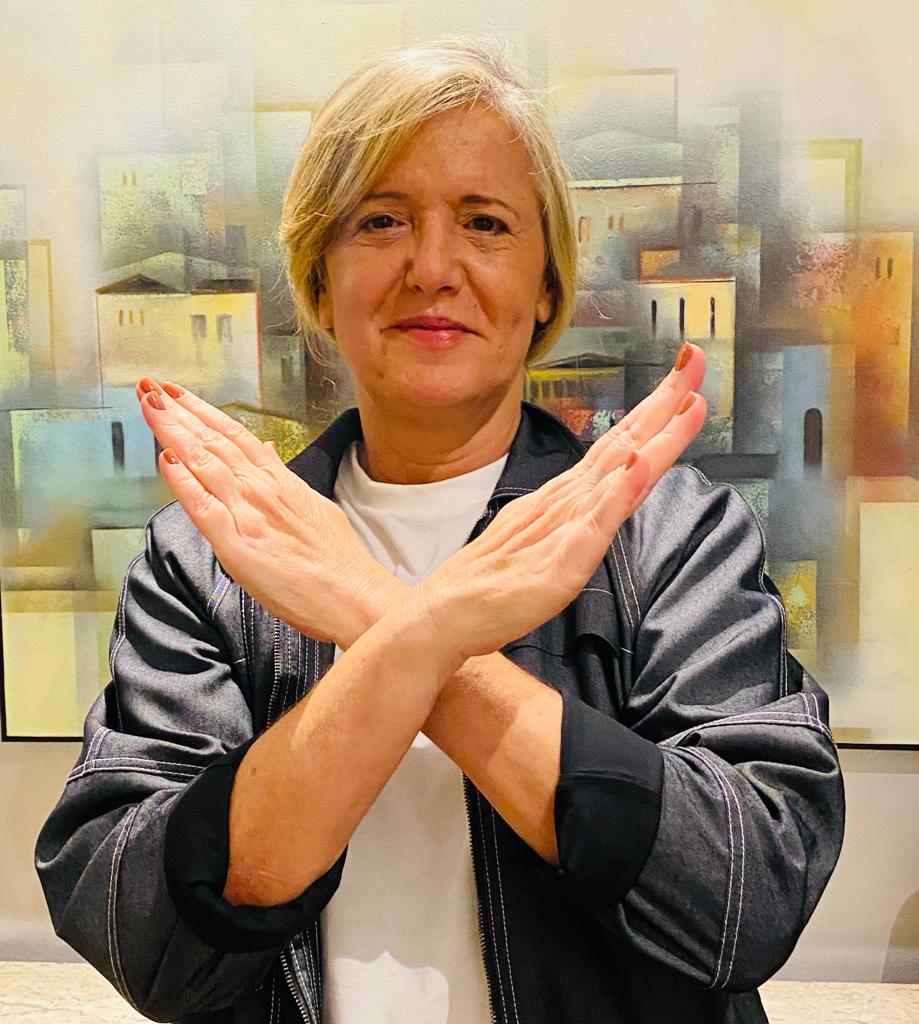 Foto da Margareth Goldenberg de braços cruzados na frente do corpo, com as mãos para cima, formando um X, gesto da campanha #QuebrandoBarreiras.