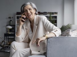 Foto de uma mulher madura falando ao telefone enquanto está em sentada em uma poltrona em um escritório.