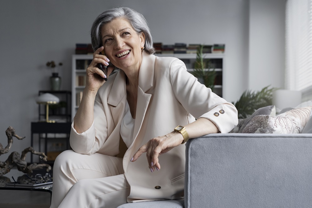 Foto de uma mulher madura falando ao telefone enquanto está em sentada em uma poltrona em um escritório.