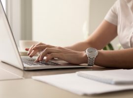 Foto em close das mãos de uma líder mulher digitando no teclado de um laptop.